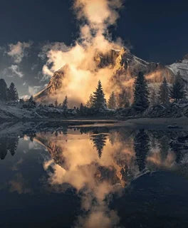 A dramatic mountain landscape in the Dolomites with snow-covered peaks, dark evergreen trees, and the reflection in Lago di Limides. A large glowing cloud rises from the mountain and is mirrored perfectly in the water.