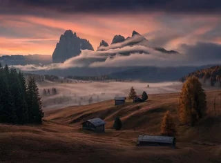 Alpe di Siusi at sunrise with dramatic clouds surrounding the mountain peaks, Mist spreads through the alpine hillside, pine trees emerge through the mist in autumn colours, and small rustic cabins on rolling hills.