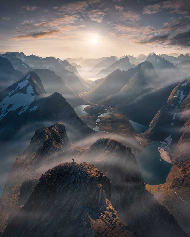 A drone photo of a man standing on a rocky mountain in Norway overlooking the fjords at sunrise near Romsdal Norway. 