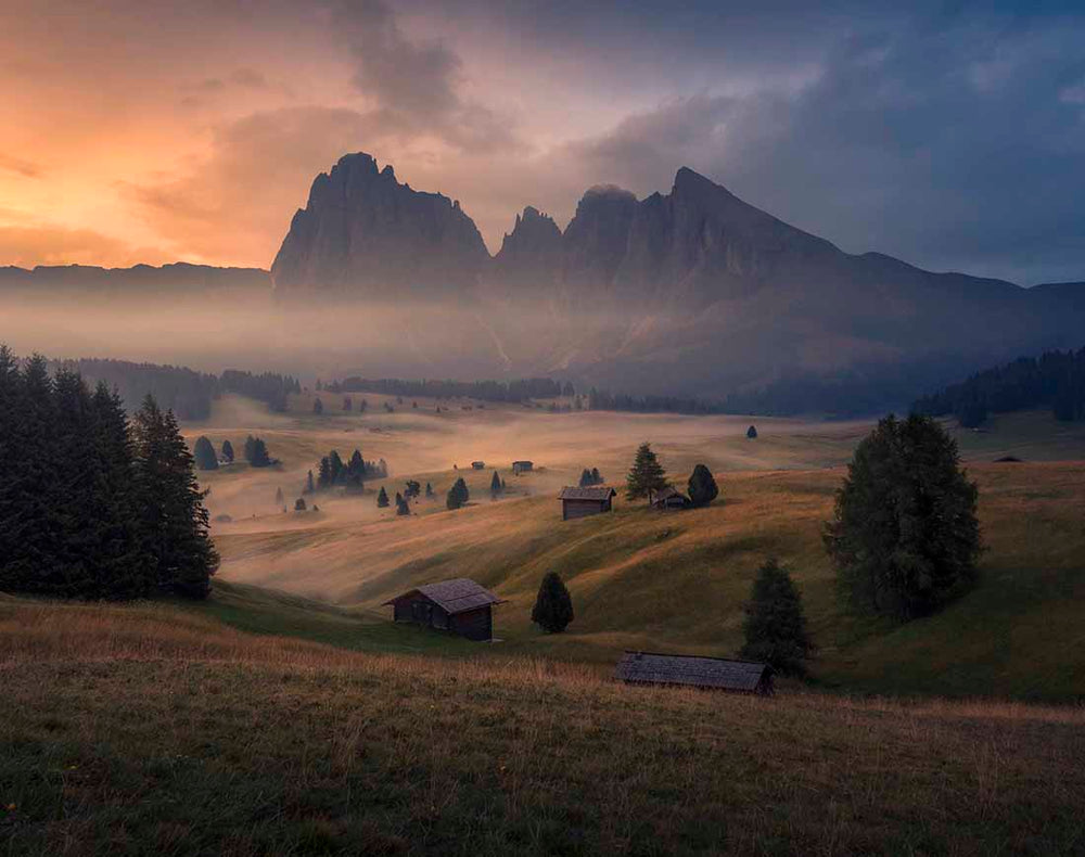 A classical composition from alpe di siusi at sunrise with mist around the mountain huts and trees in autumn.