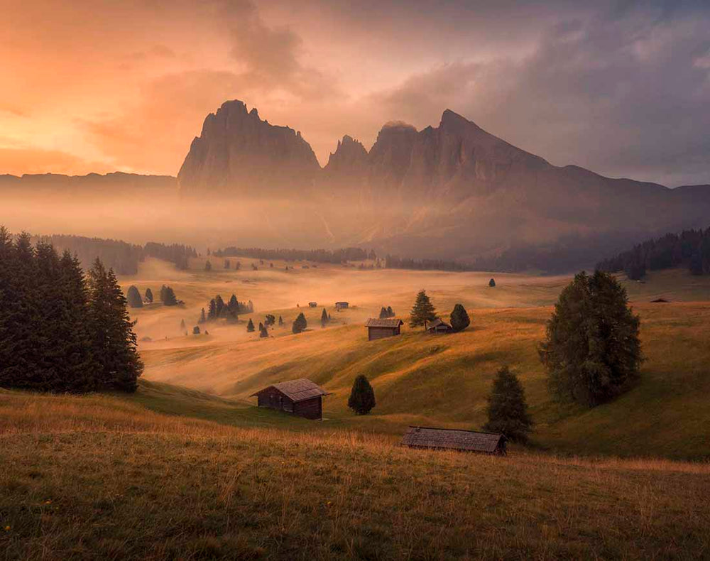 A classical composition from alpe di siusi at sunrise with mist around the mountain huts and trees in autumn.