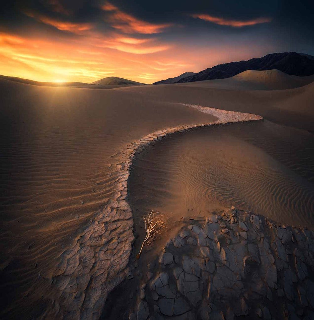 mud cracks form a leading line to the golden sunrise in the death valley national park in the USA