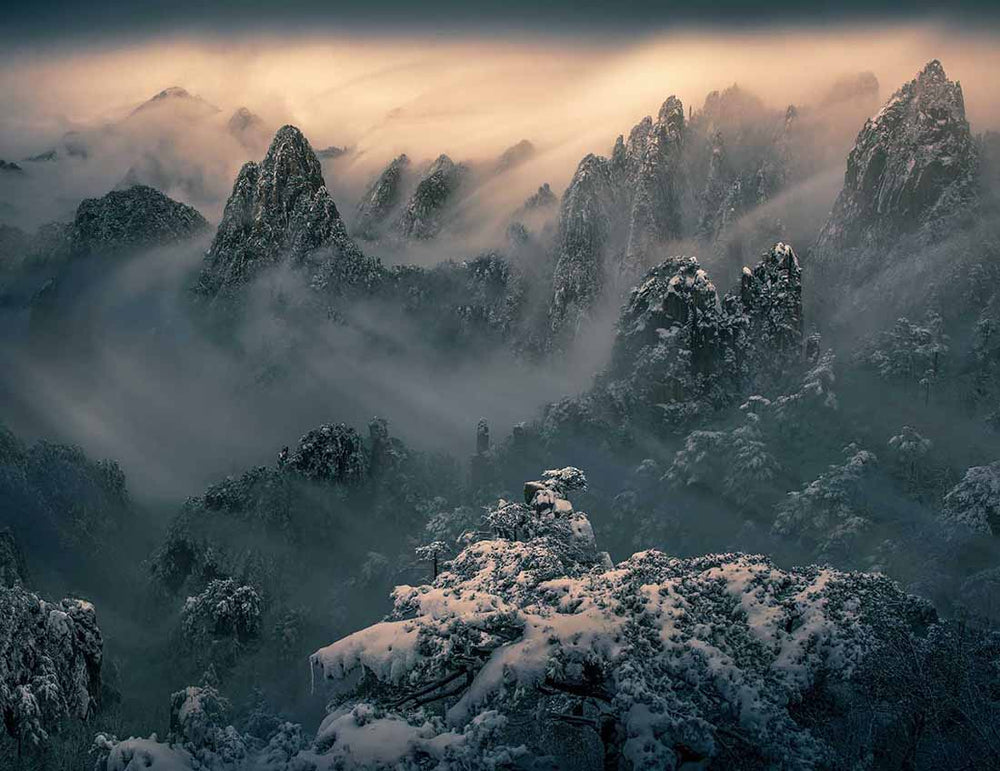 Layers of large snowy misty mountains at sunrise in China.