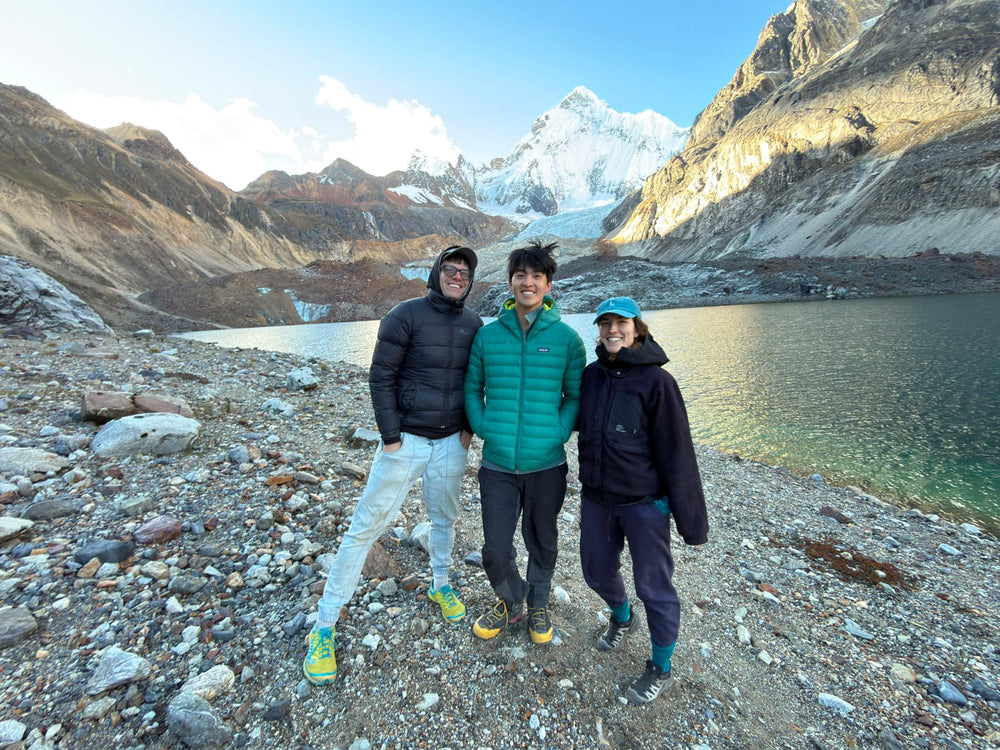 Three people, Max Rive, Forest Kai and Madison McCardle stand together in Cordillera Huayhuash in Peru beside a lake.