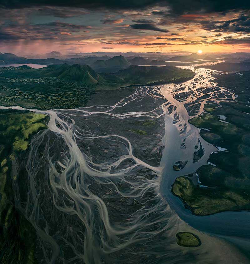 Landmannalaugar aerial view at sunset where all the different glacier streams weave together and create leading lines to the glowing sun on the horizon.