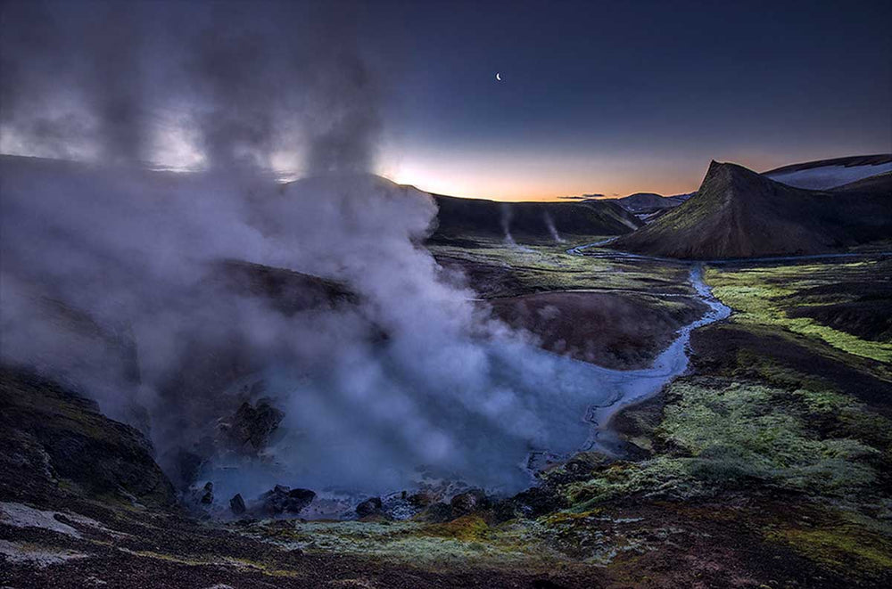 Landmannalaugar at night time with mist and cloud. In the foreground is a large lake and stream leads from the lake to the mountain behind.