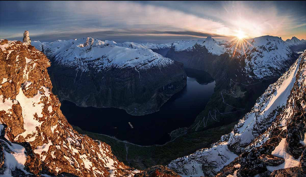 Laushornet overlooking Geirangerfjord. All the fjords are covered in snow, in the distance a sunstar forms over one of the peaks.