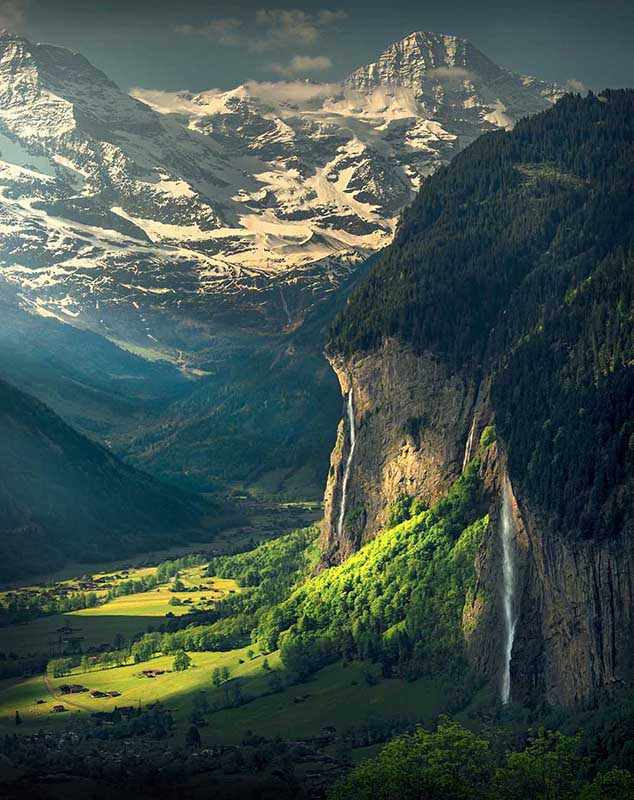 Spissbachfall and Staubbach falls in the village of lauterbrunnen can be seen in summer green hillsides. Snow capped mountains in the distance.