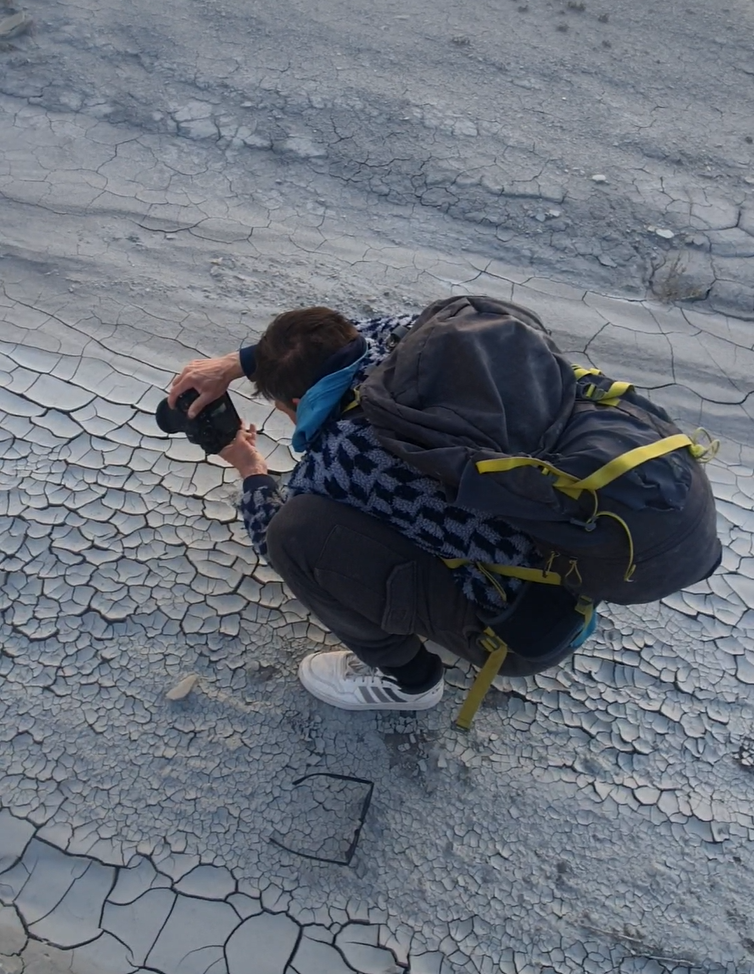 man crouches to photography mud-cracks as foreground in utah.