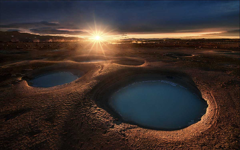 Theistareykir at sunset in Iceland. A sunstar shines golden on the horizon. In the foreground the giant blue pools great pockets across the flat land.