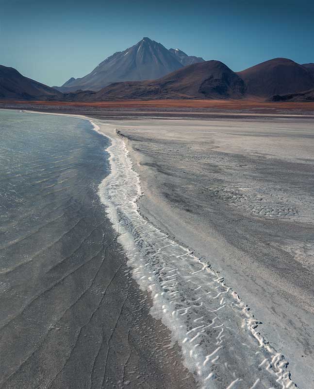 salt lines lead toward a distant volcano in the Atacama desert.