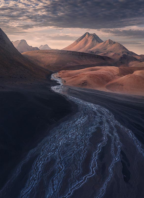 small salt streams lead in the desert valley towards a volcano in the background at sunrise.