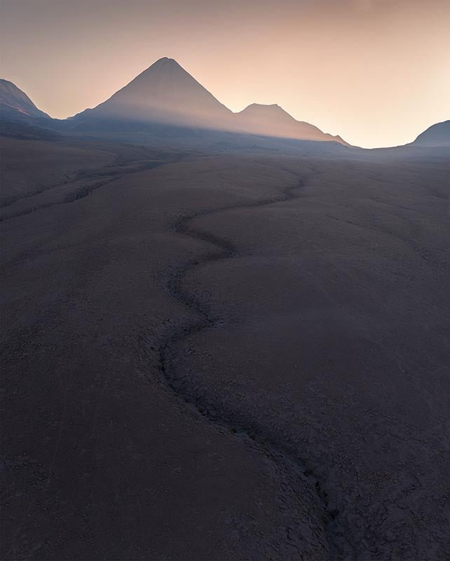 a giant crack and mud stream leads to a volcano at sunrise in the Atacama desert.
