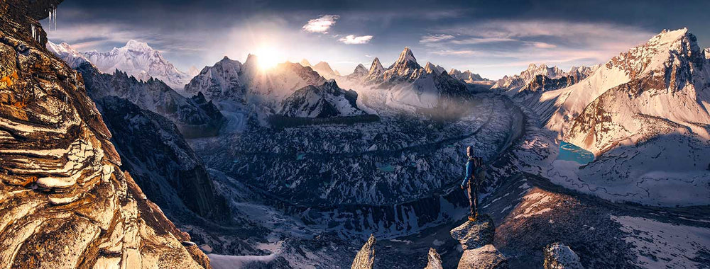 Himalayas of Nepal panorama from a high view point. man stands on a rock on the edge of a ridgeline looking into the sunrise. Snow covered peaks and glacier rivers surround the scene.