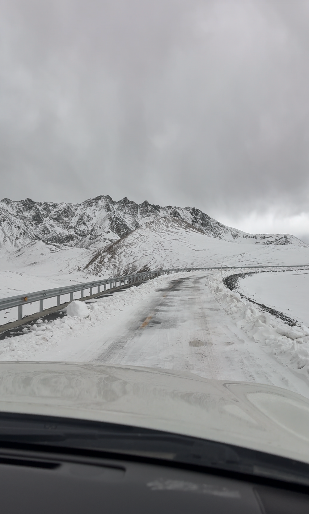 A snow covered road in Tibet with snowy mountains all around it and a clouded sky.