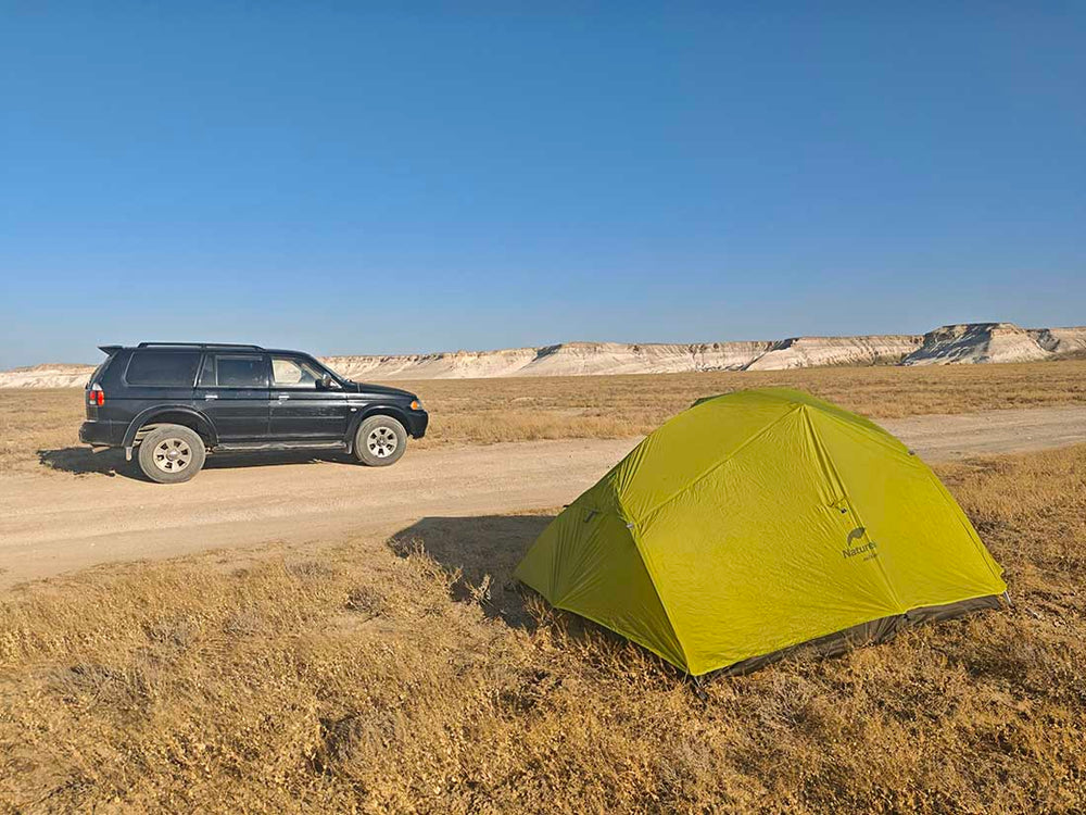 a green tent is pitched in the desert steppe in kazakhstan in front of a 4x4 car.