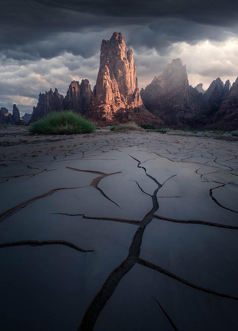 cracked mud creates leading lines towards a rocky mountain in Saudi Arabia at sunrise.