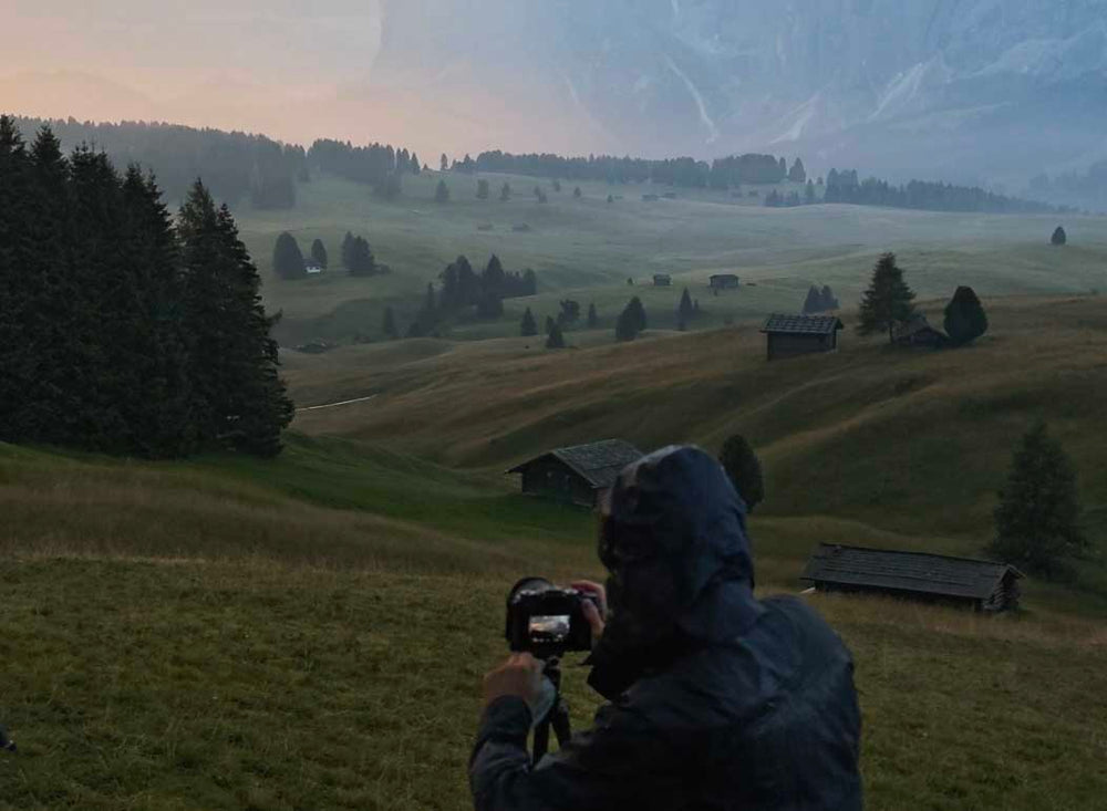 alpe di siusi mountains at sunrise with mist and mountain huts, a man takes a photo of them.