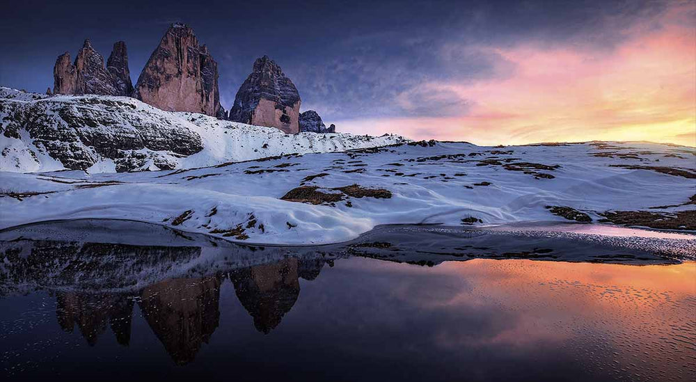 A panorama shows golden coloured sunset over snowy fjords with high mountains in the background in Dolomites.