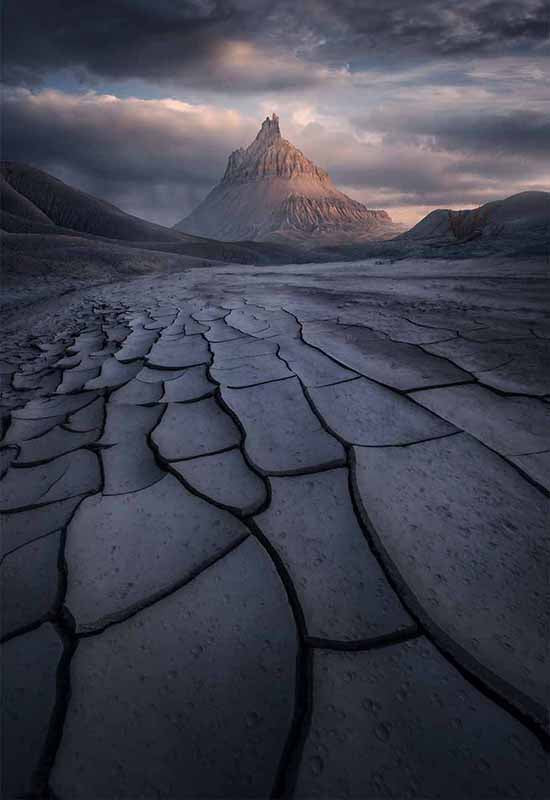 Factory Butte in the USA during sunset as it catches the pink glow of evening light. Beneath it the mudcracks are large and form a river of lines pointing to the mountain.
