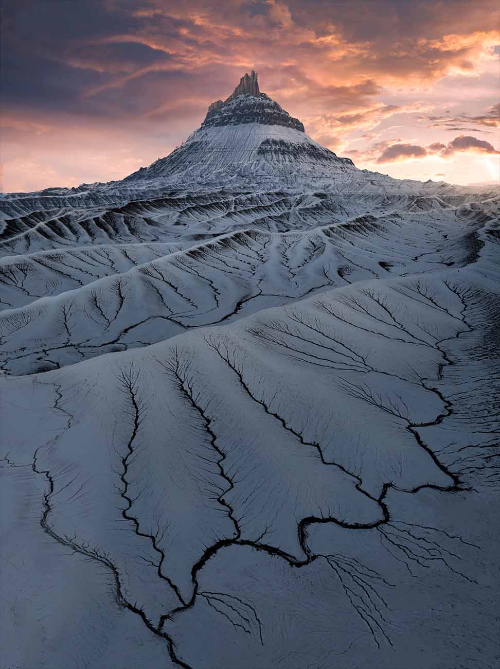 Factory butte at sunset in orange golden light winter time. Giant dunes of mud valleys are covered in snow creating unique leading line patterns.