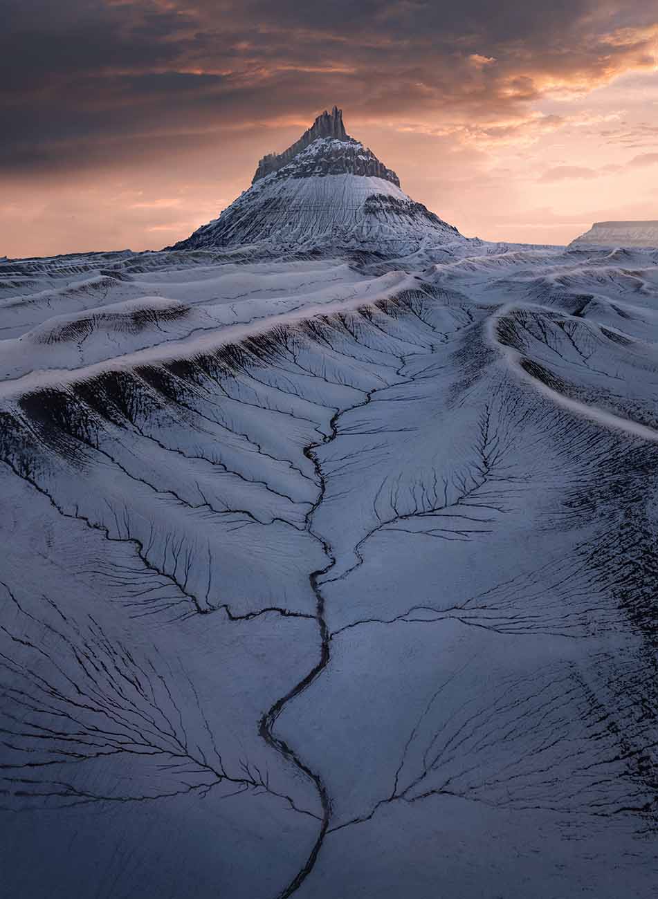 factory butte in the southwest USA during a pink sunset. Snow covers the mountain and mud dunes creating floral patterns in the mud.