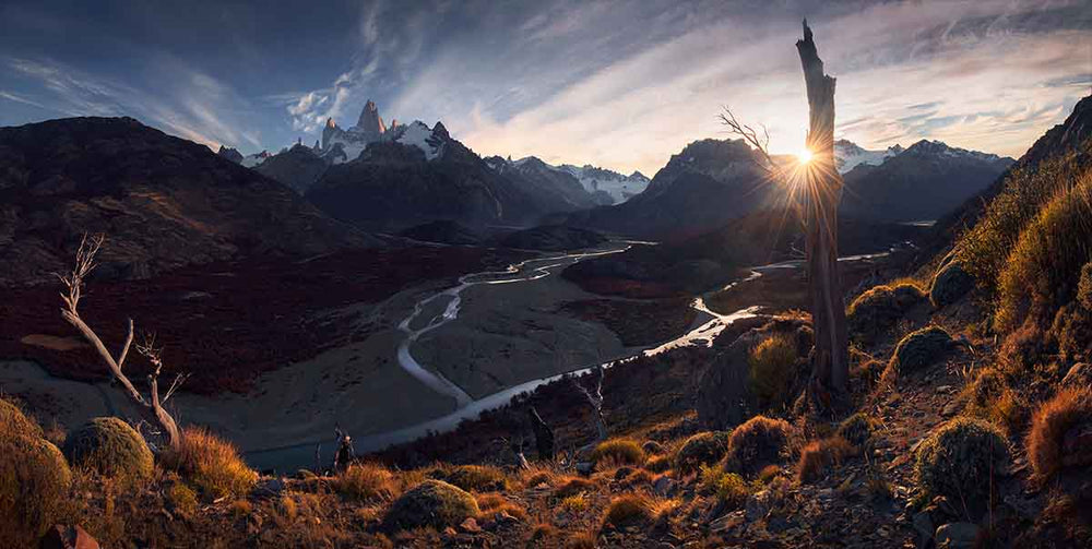 a stunstar is golden and winding rivers lead to mountains in the distance.