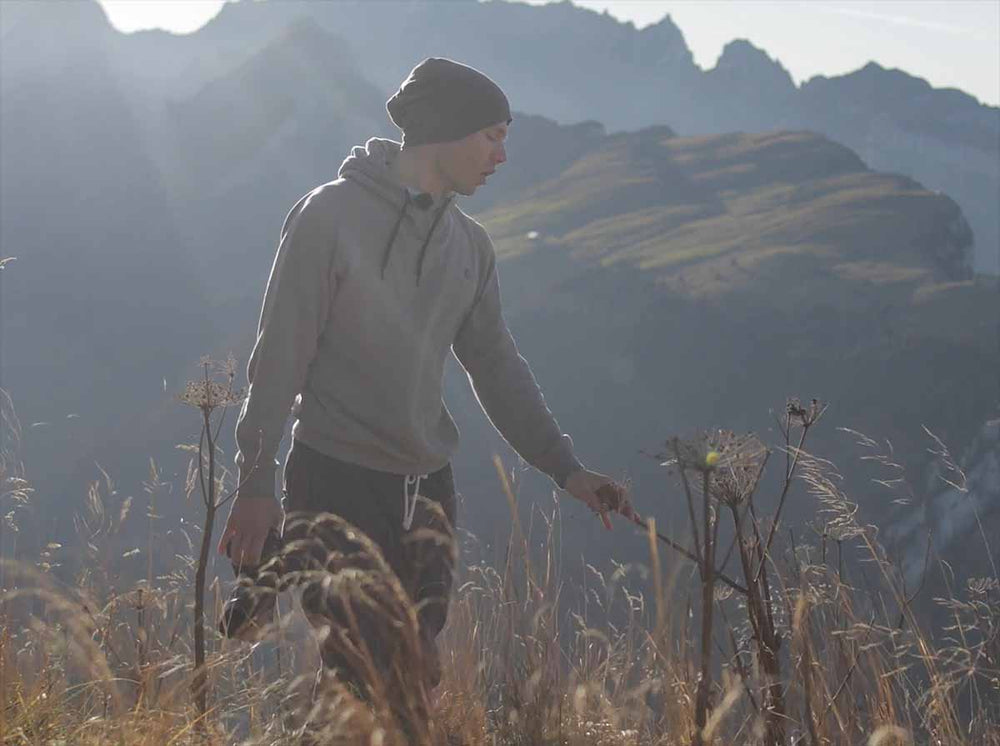 A sexy man stands in a field of grass on high mountains.