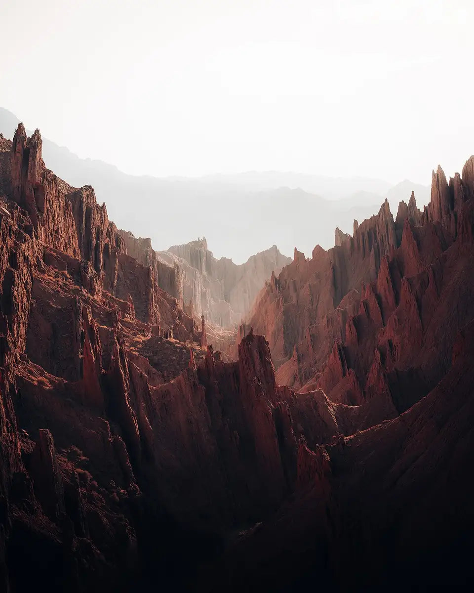 Layered sharp rocky peaks of red stone landscape in Xinjiang, China, soft light illuminates the background peaks creating separation.