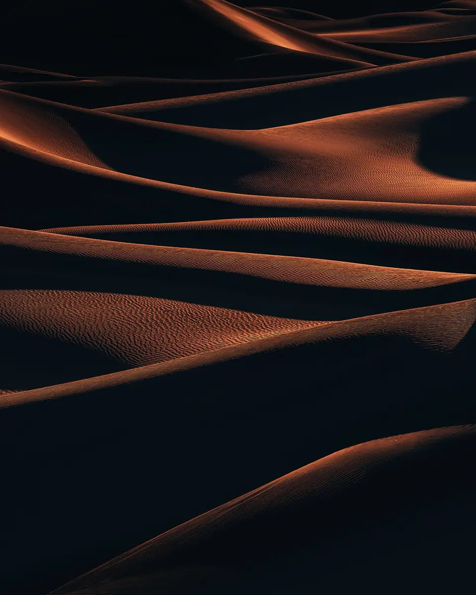 Death Valley in the USA with layers of sand dunes far into the distance creating an abstract scene where golden light illuminates the ridgelines.