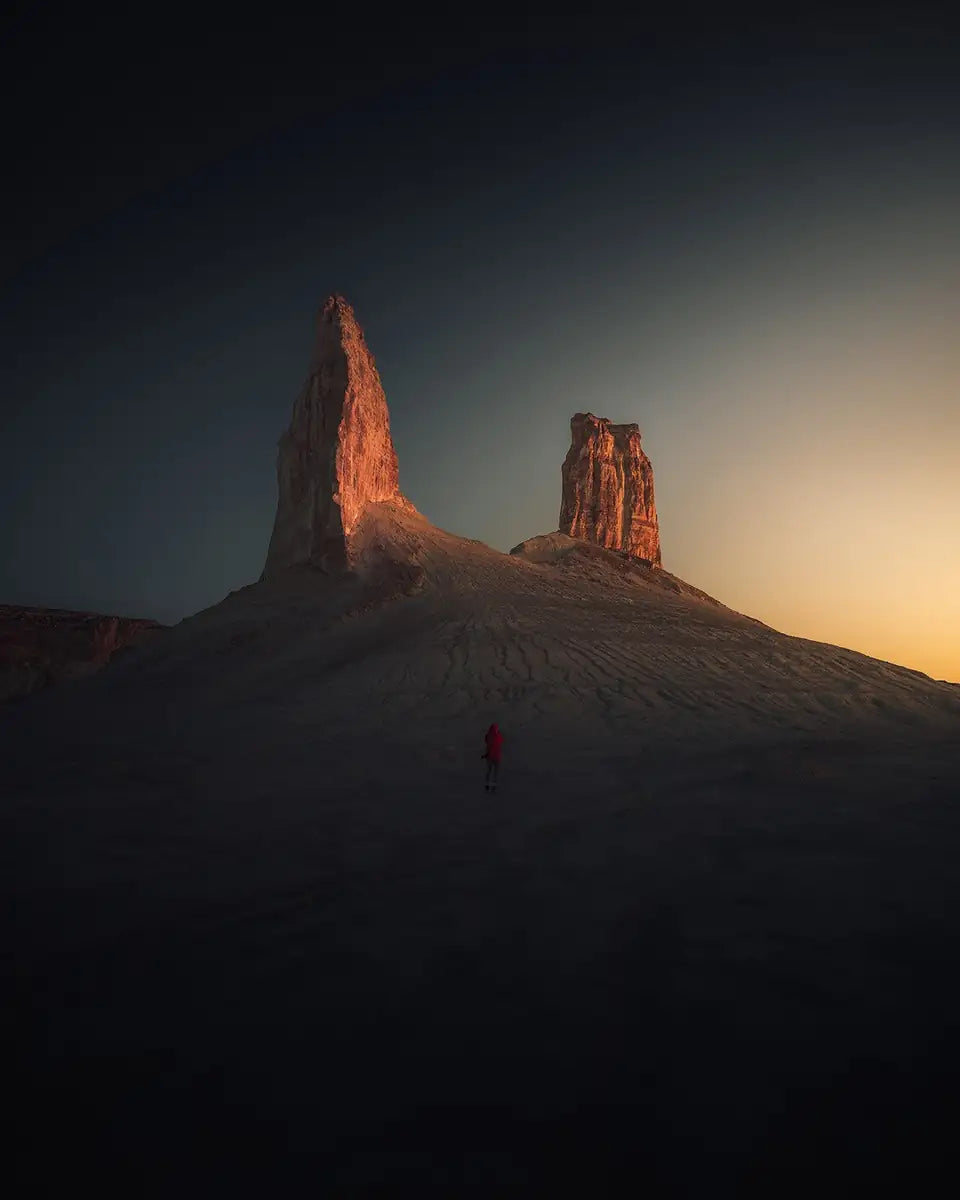 A Person in a moody Kazakhstan landscape underneath two peaks catching golden sunset light.