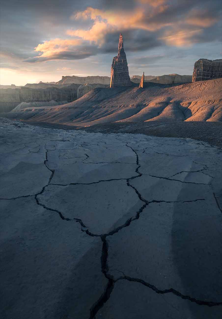 the sharp spire of long dong silver in the southwest USA at sunset. Pink and golden light illuminates the mud dunes. Giant cracked mud points towards the peaks.