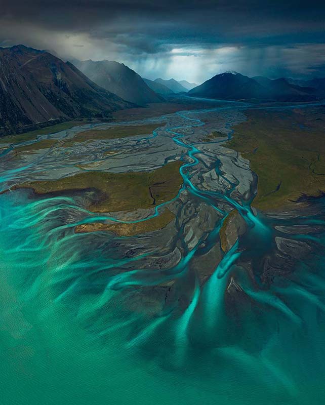 The beautiful blue lines of a glacier lake flow into a stream which runs across the valley floor in New Zealand and between giant mountain ranges. Lake Tekapo.