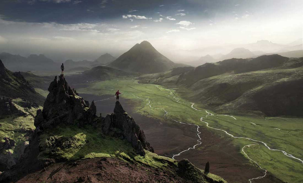In Iceland two men stand on pointy rocks in landmannalaugar overlooking the rivers and mountains. Taken by drone.