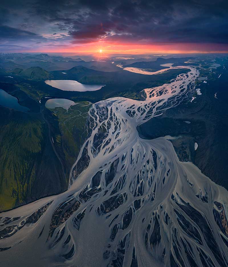 landmannalaugar in Iceland at sunset taken from an aerial perspective. The rivers intertwine together forming an intricate pattern which leads to the orange sun on the horizon.