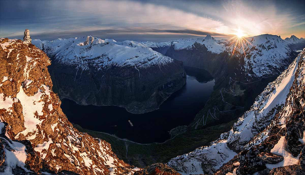 A panorama over Norways fjords between snow capped mountains at sunset.