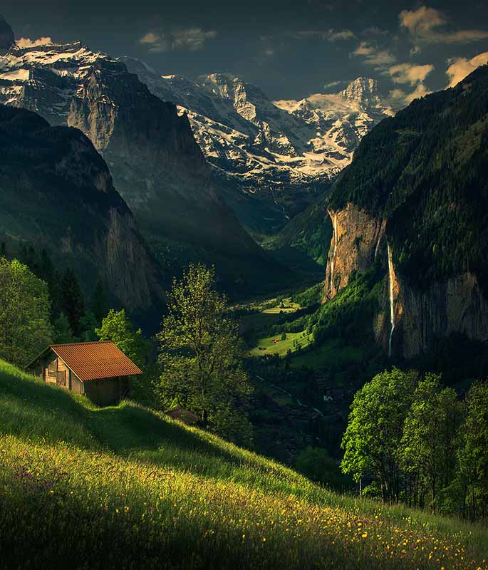 a mountain hut on a green mountainside, waterffalls run down the cliffs in the background to lauterbrunnen village below.