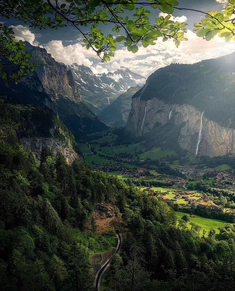 taken from high up you can see the village of lauterbrunnen in the valley in summer. three waterfalls come down the side of the cliffs to the valley below.