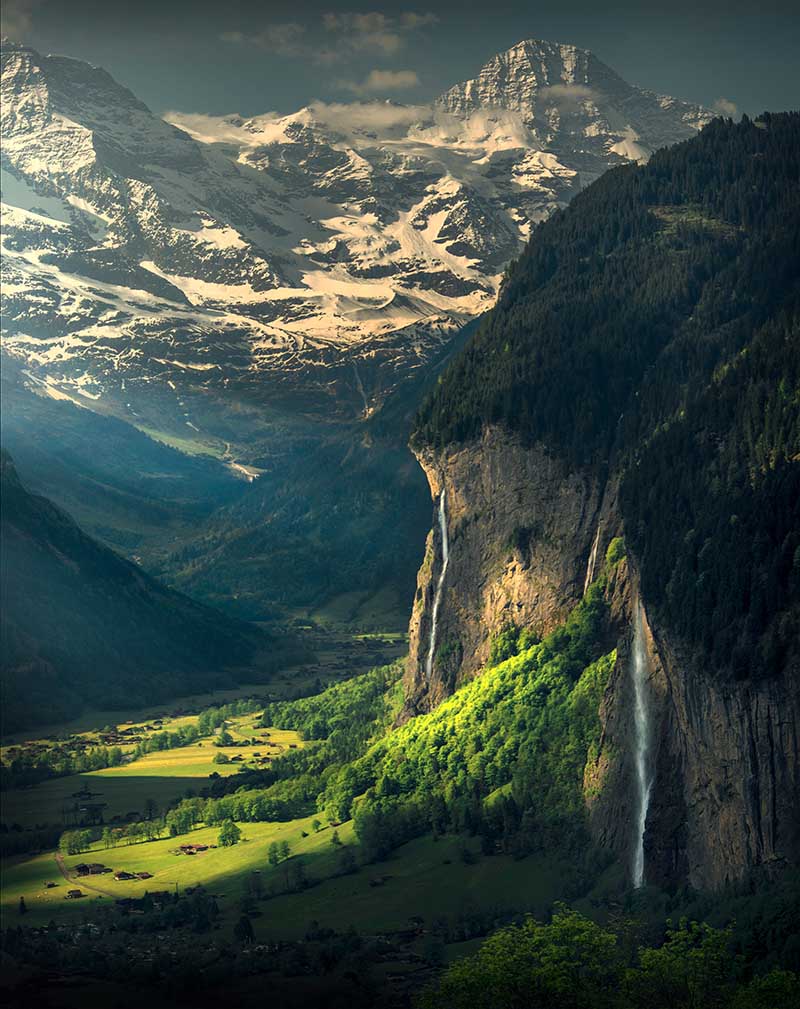 sunrays pour into the valley of lauterbrunnen, the waterfalls of staubbachfall is seen pouring into the green mountain below.
