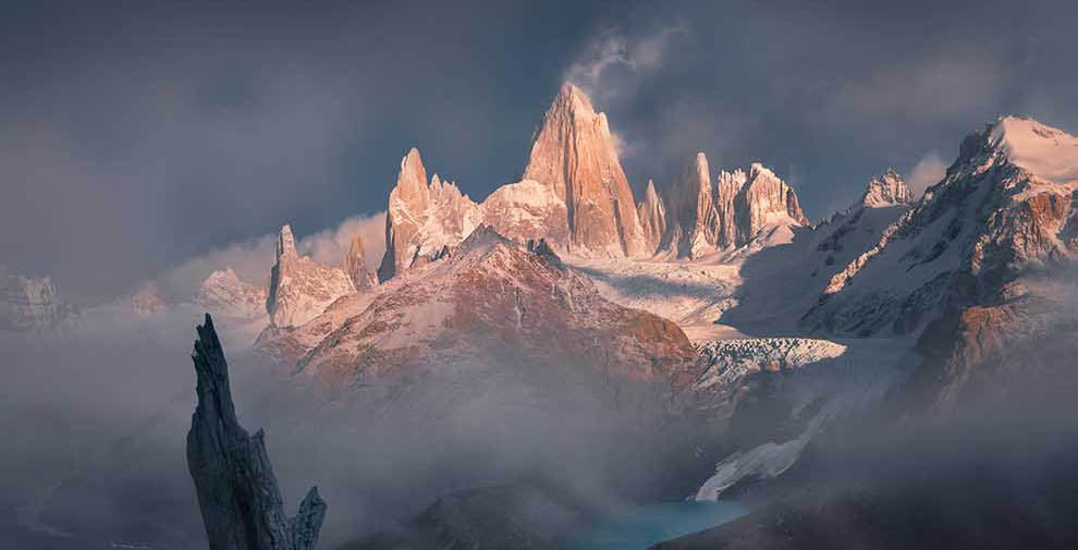 A stark winter tree creates a leading line to the sharp snow covered mountains of Mont fitz roy in Patagonia during a sunrise.