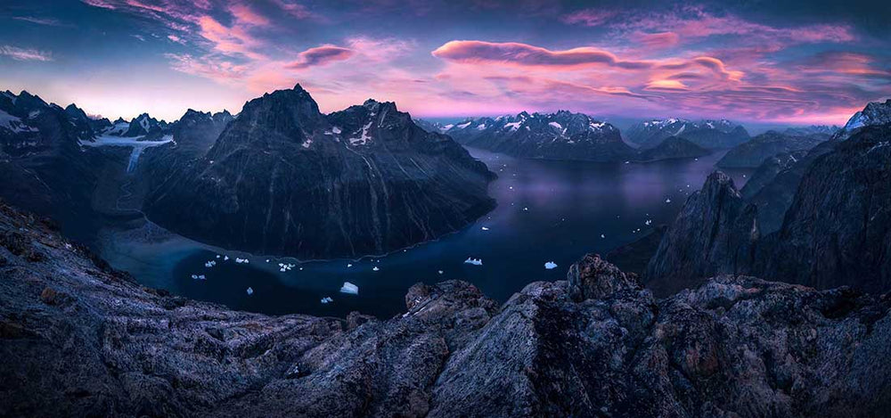 lenticular clouds over the fjords of Greenland snow and glaciers in the mountains and a pink sunset from high viewpoint.