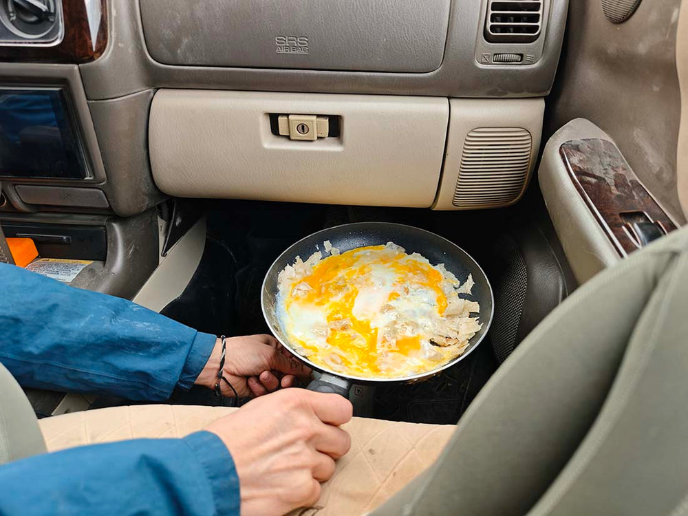 max rive cooking eggs in the front seat of a car in Kazakhstan using his gas burner.