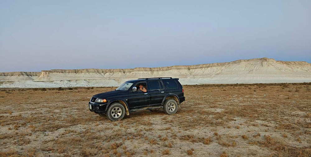 max rive in a 4x4 vehicle in the steppe of Kazakhstan with white cliffs in the distance.
