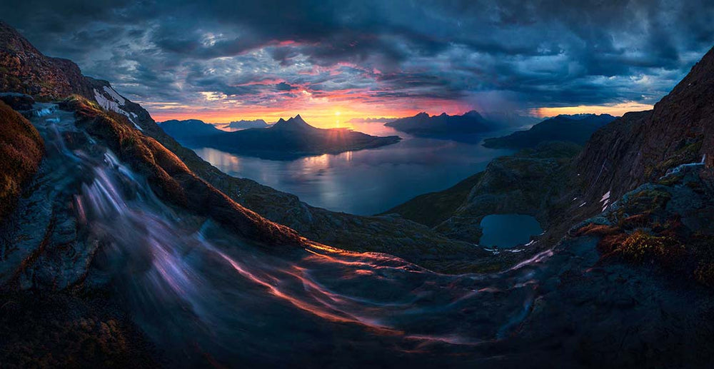 a waterfall on a high mountain overlooking a pink and yellow sunrise and fjords in norway.