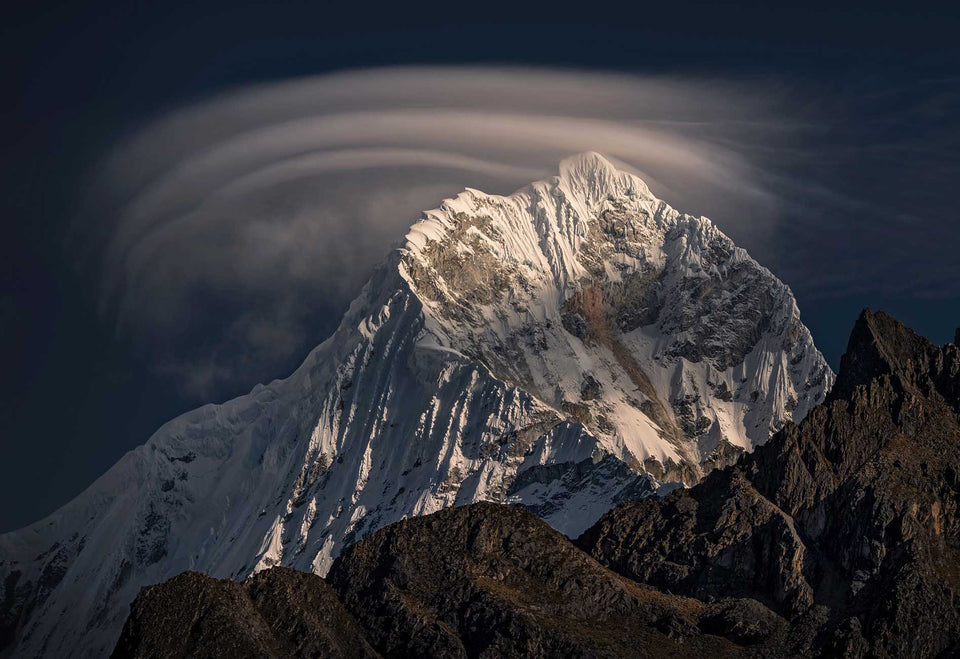 A snow-covered peak beneath a large wave-shaped lenticular cloud in Peru.