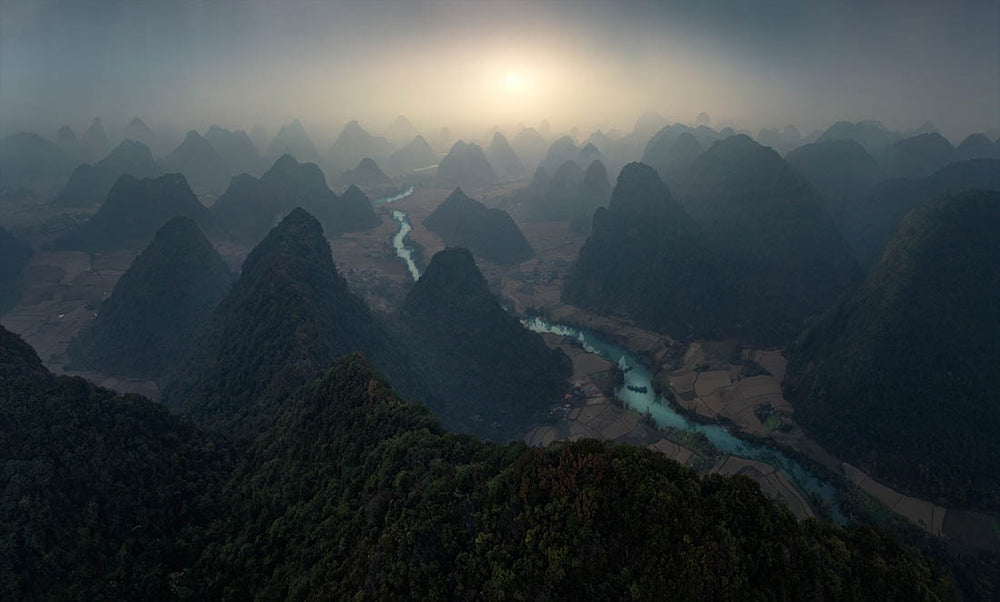 a drone view of north Vietnam mountains at sunrise with an ultra blue river winding through the dome shaped hills.