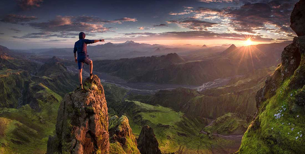 Max Rive stands on a mountain in thormsmork at sunrise pointing to the sunstar over the valley.