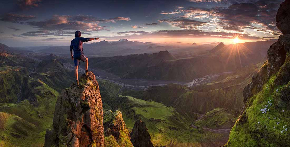 man stands on high rocky mountain pointing to the sunset over the valleys of thormsmork.A river flows between the mountains.