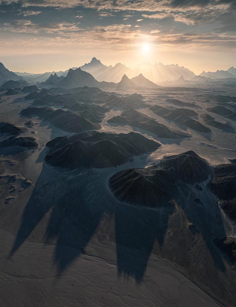 An aerial view of ridged desert hills and long shadows beneath the low sun in Saudi Arabia.