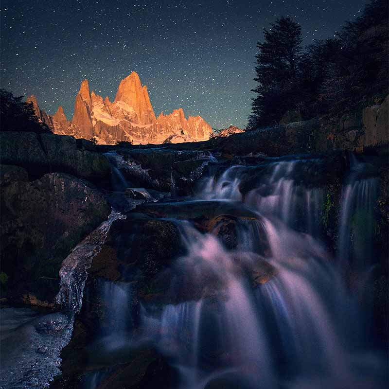 monte fitzroy under the night sky, a large waterfall cascades in the foreground.